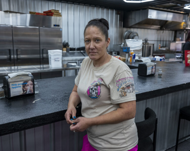 A woman leans against a table inside a building.