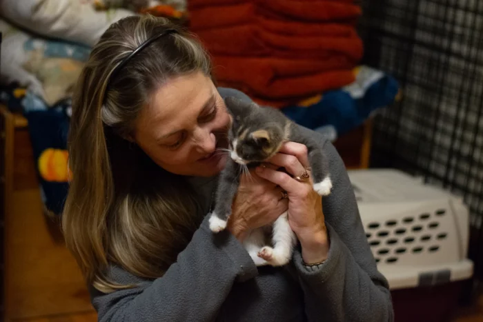 A white woman holding a kitten that has white, gray and tan fur. 