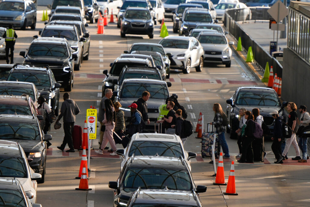 A multi-lane interstate is crowded with cars and trucks. Emergency workers are on the scene of an accident in the right two lanes that is forcing drivers to merge into fewer lanes.