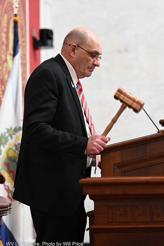 A man stands at a podium looking down and using a gavel.