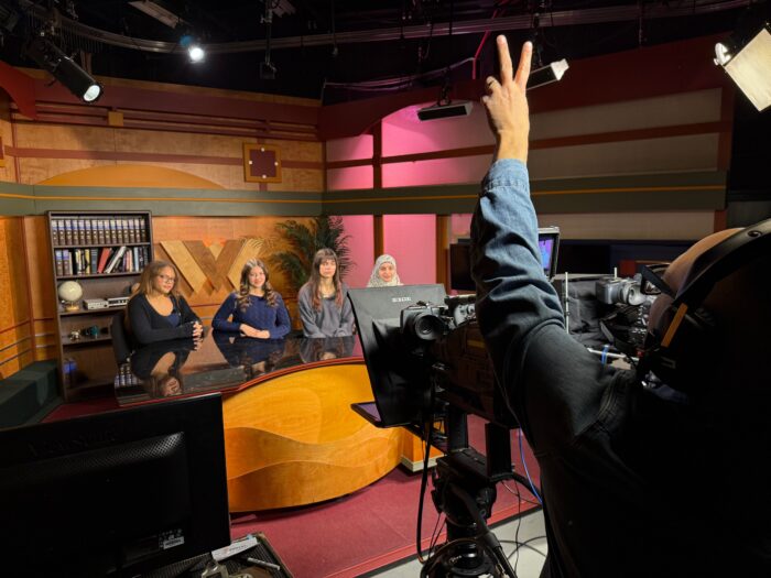 Four young women in high school sit on the set of a TV studio.