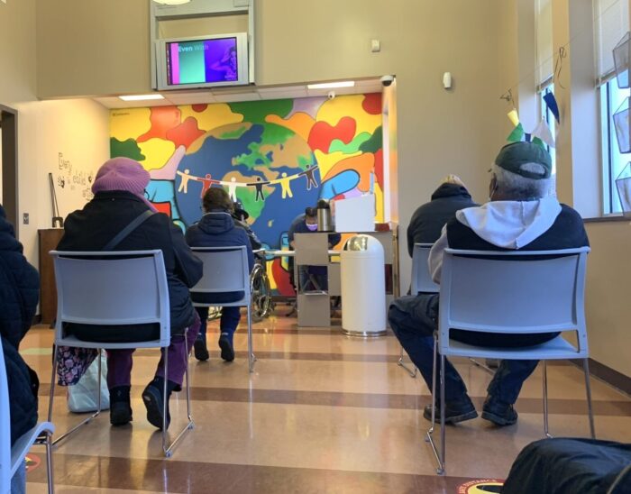 People sitting in chairs in a waiting room. Their backs are turned to the camera.