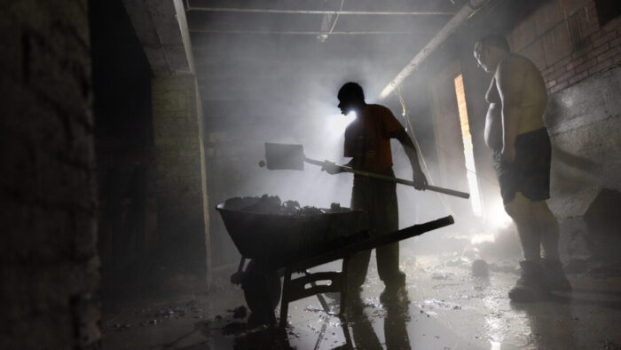 Two men scooping debris with a shovel into a wheelbarrow.