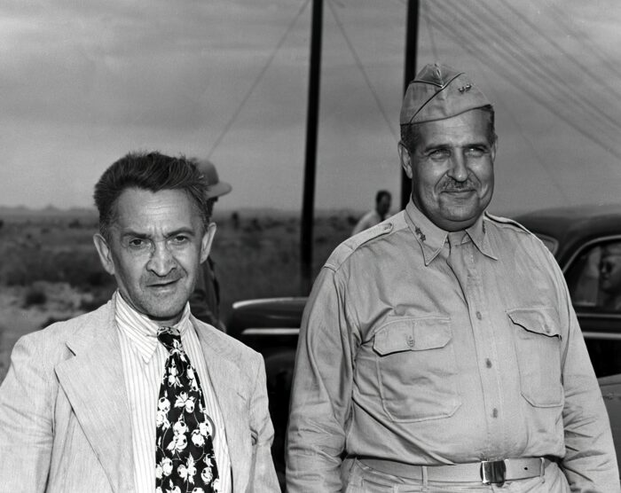 A black and white photo of two men standing outside. One of them is wearing an army uniform and the other is wearing a suit with a patterned tie.