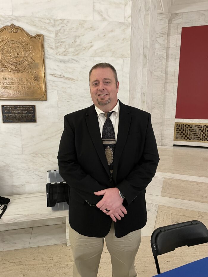 A middle age man stands inside the West Virginia Capitol building. He is formally dressed.