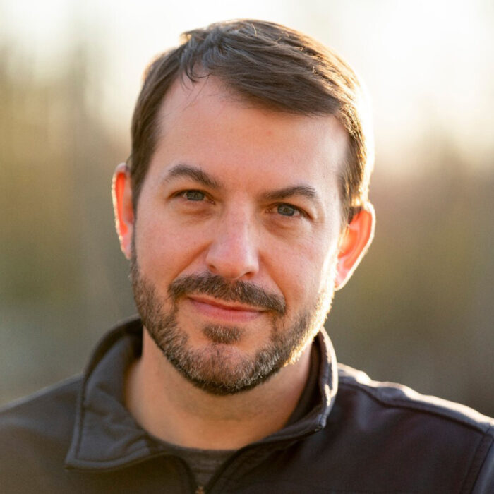 A portrait photo of a white man. He has brown hair and is wearing a black quarter zip.