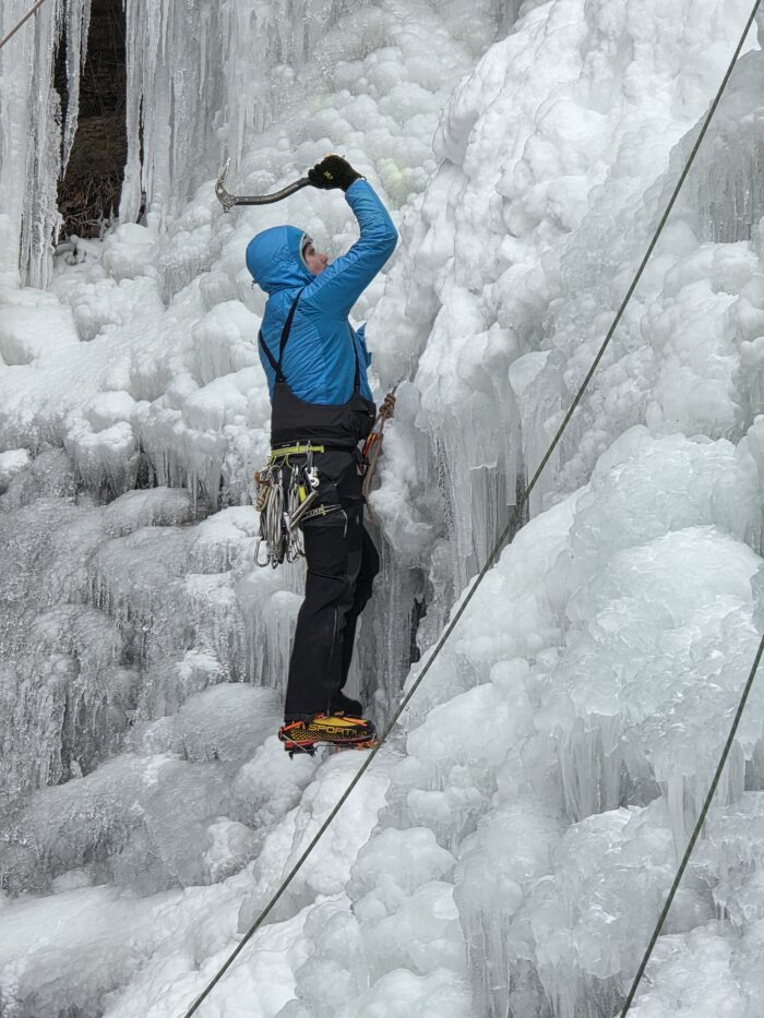 man in blue coat climbs ice