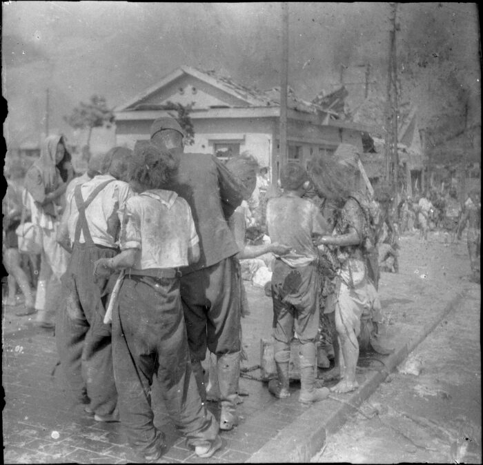 A black and white photo where people are turned away from the camera and looking at something. They are covered in debris. 