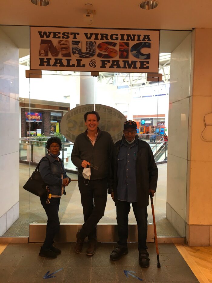 Three adults stand in front of glass doors. Above them is a sign that says, "West Virginia Music Hall of Fame."