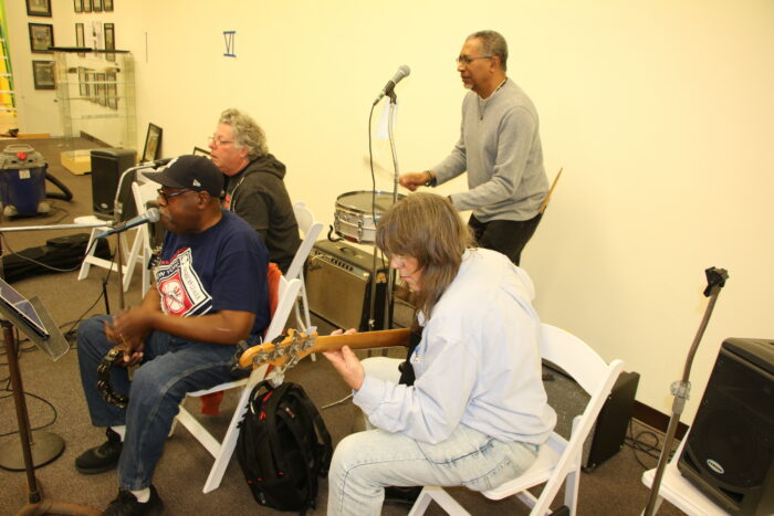 Four adults playing musical instruments practice.