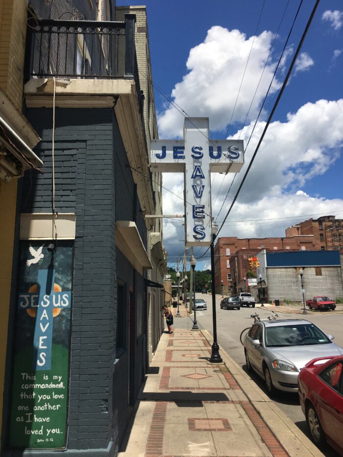 Outside a building on a mostly sunny day with a sign in the shape of a cross that reads "Jesus Saves."
