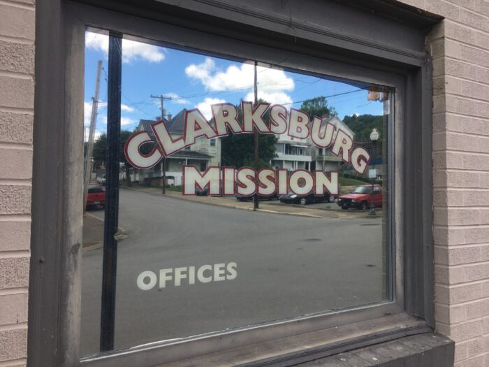 Outside of a window. The window has words printed on it that read, "Clarksburg Mission."