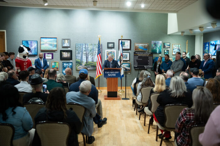 Crowd seated looking at a gray haired man at a podium
