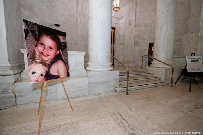 A large image of a smiling girl holding a doll is displayed on a stand outside of the steps to a wooden door framed by marble columns.