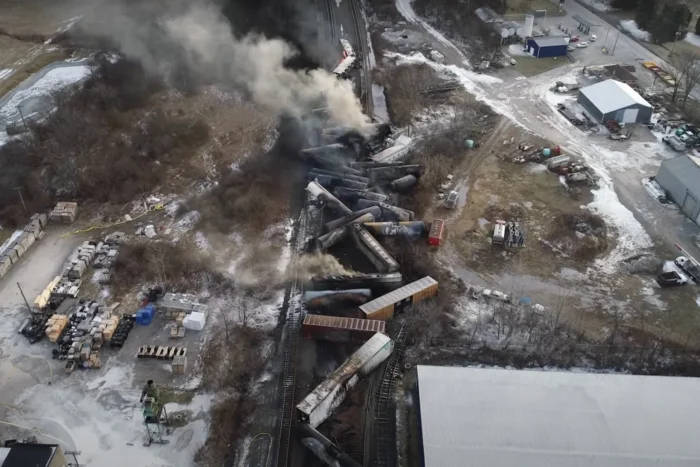 An aerial photo of a train derailment. There are train cars crashed into each other and smoke is pouring into the atmosphere.
