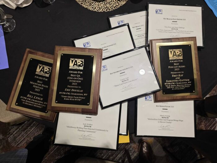 Pile of award plaques and framed awards lay on a table covered by a black tablecloth