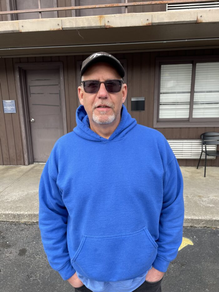 Man in a blue hood, hat and sunglasses looks at the camera