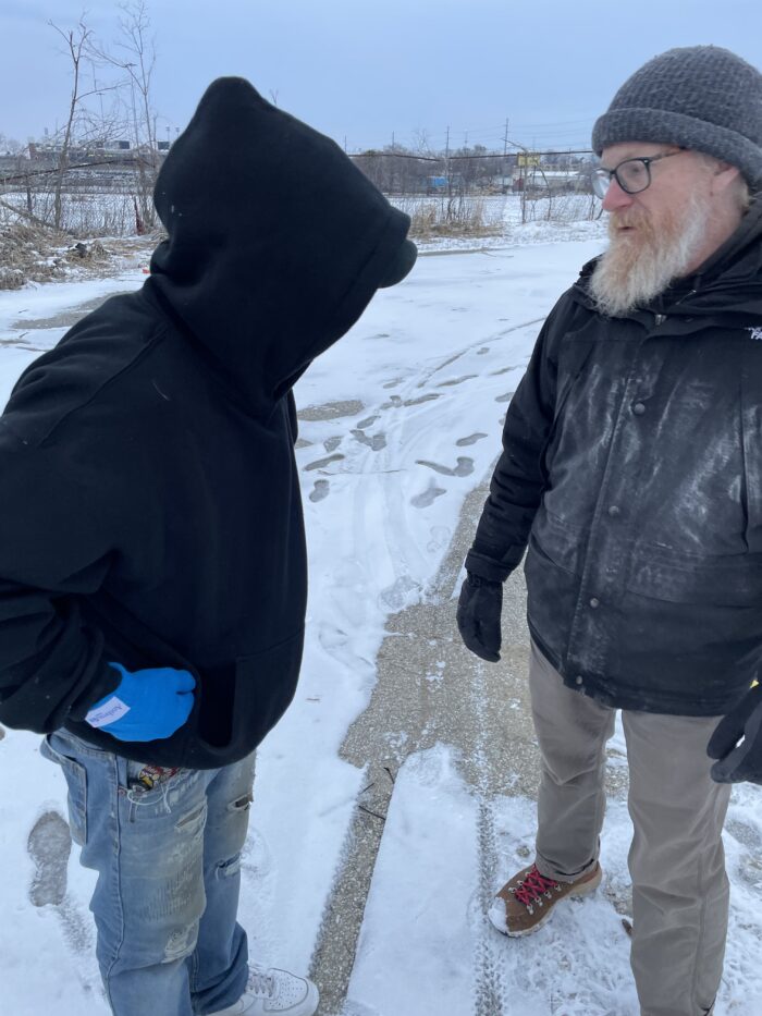 two men standing in the snow and cold, one facing away from the camera