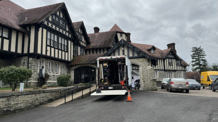 An equipment truck is parked in front of a large expensive looking cream colored building with dark wood planks.