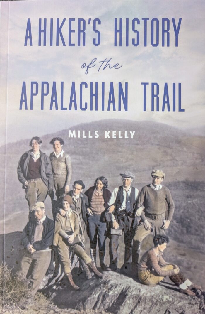 The cover of a book with the title, "A Hiker's History of the Appalachian Trail" by Mills Kelly. There is a photo of nine people posing on the Appalachian trail. 
