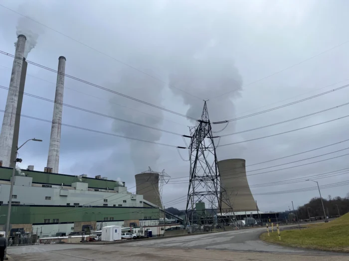 A ground-level view of a coal-fired plant. There are three smokestacks and two cooling towers behind the factory building. 