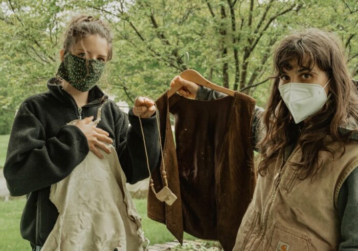 Two people holding buckskin clothing. They're both wearing face masks, and they are standing outside.  