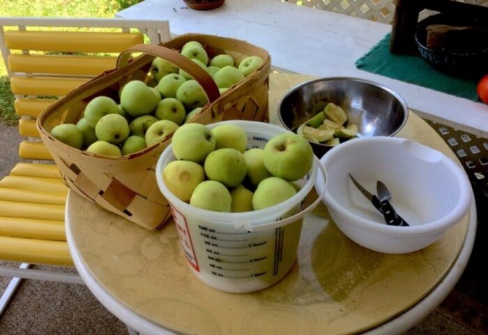 Green apples sitting in a basket on a table. 