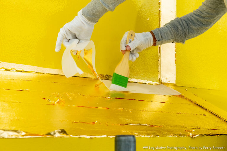 Hands wearing gloves carefully paint gold leaf onto the capitol dome in Charleston, West Virginia.