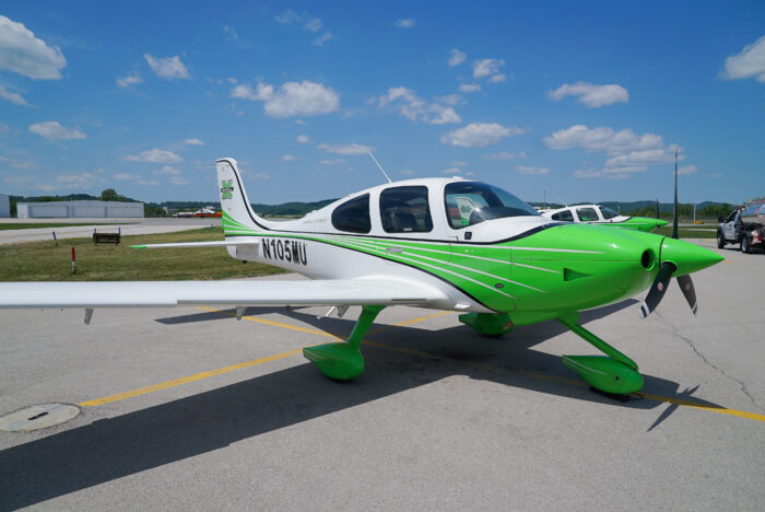 A white and green propeller plane sits under blue skies on a tarmac