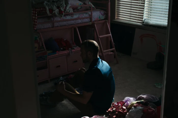 A man sitting in a dark room. He is facing away. 
