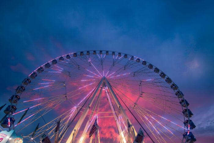 A large Ferris wheel is silhouetted against a pink and blue evening sky.