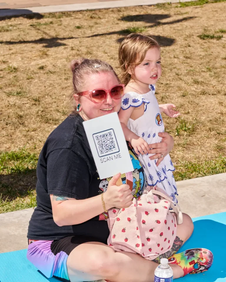 A woman and a young girl together on a yoga mat outside on a sunny day.