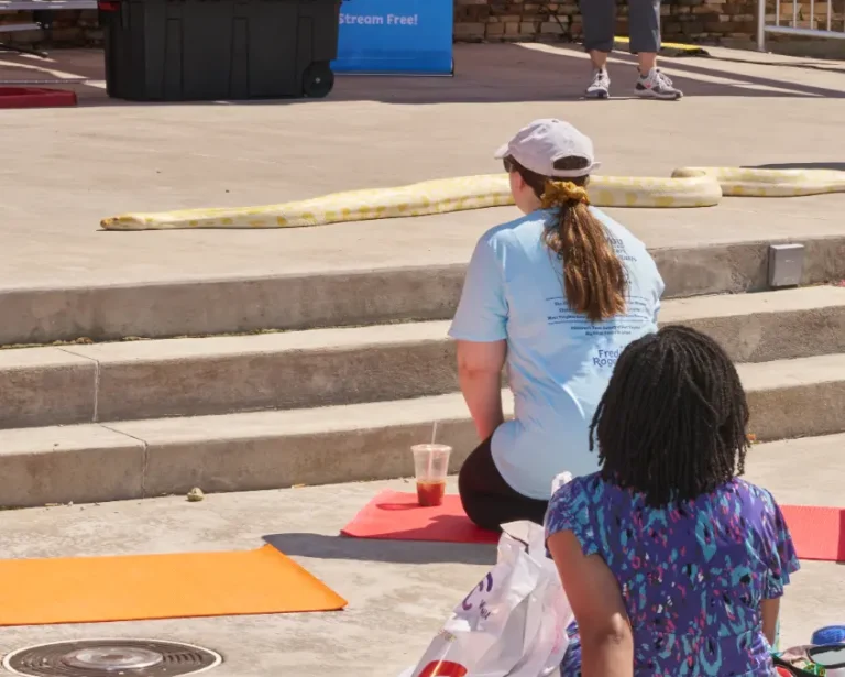 Two people watch a snake slither along on a concrete stage.
