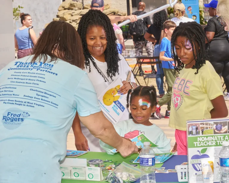Four people, two adult women and two young girls. They stand at a vendor table and look at the variety of items on the table.