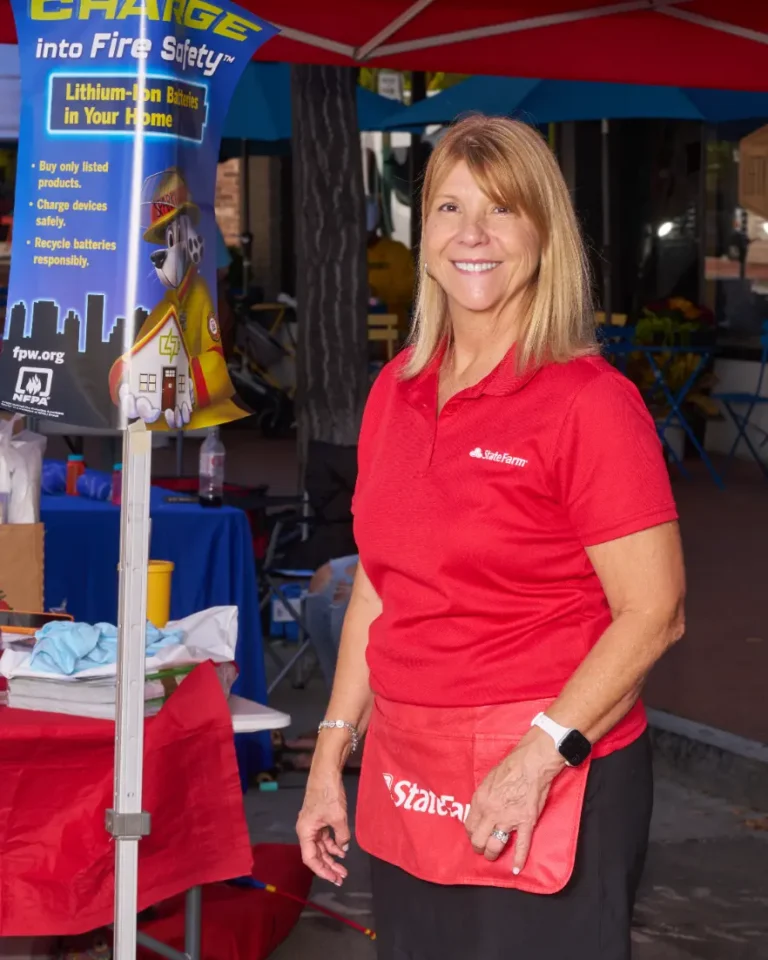An adult woman with blond hair and wearing a red shirt looks toward the camera and smiles.