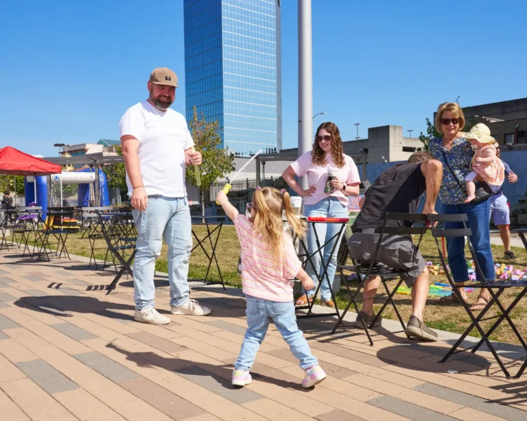 Six people are visible. Two adult women, two adult men, and two small children. They are playing together, smiling on a sunny day.