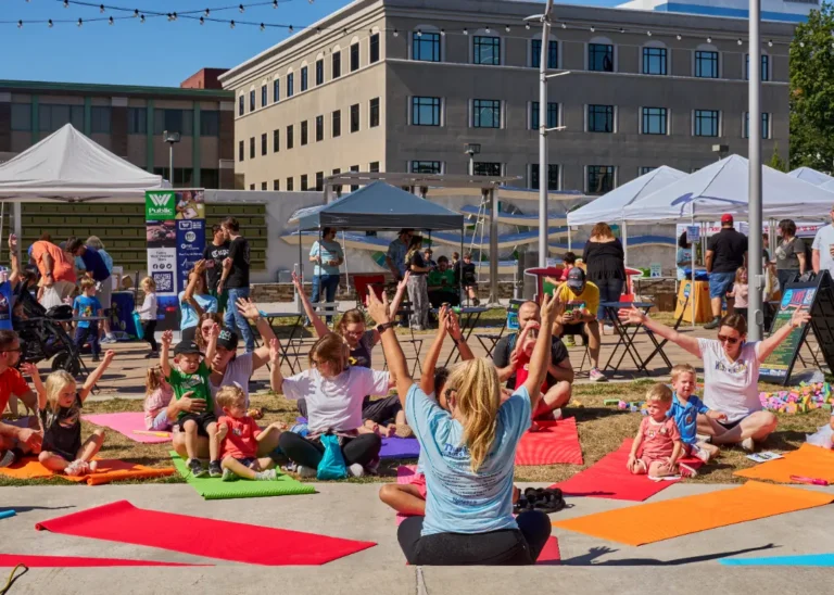 Several people, adults and children, do yoga outside on a sunny day.