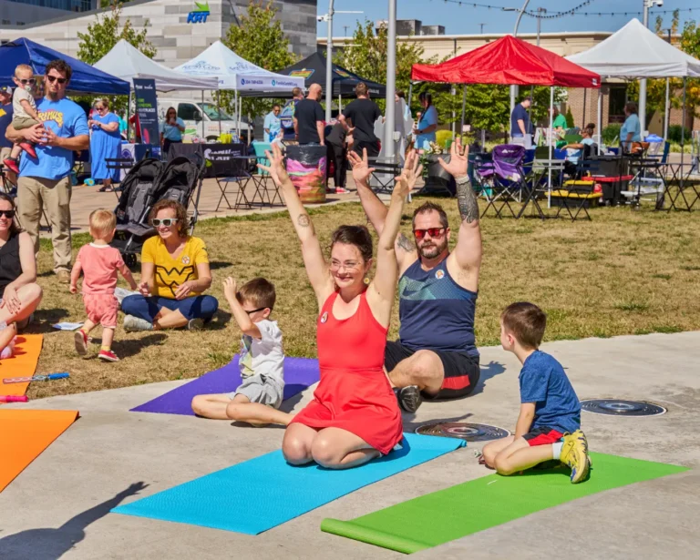 Two adults and two young boys are seen doing yoga outside on a sunny day.