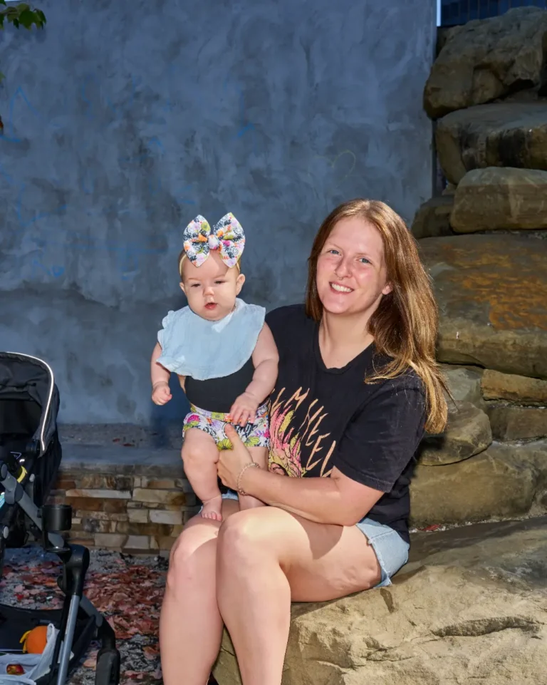 A mother holds her small baby. The baby is wearing a large bow.