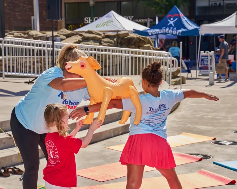 A young girl does yoga while balancing a balloon dog on her shoulder.