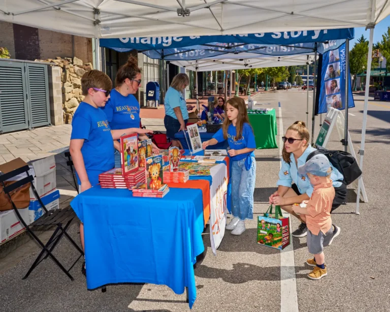Four adults are visible and two children. The stand next to a vendor table where several books are stacked.