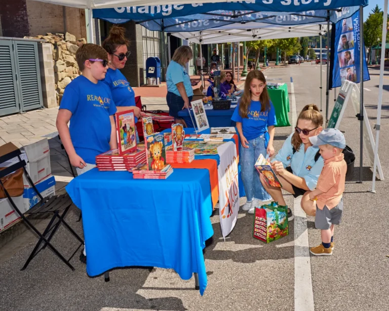 Four adults are visible and two children. The stand next to a vendor table where several books are stacked.