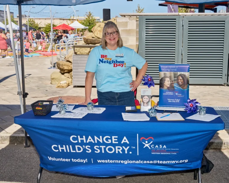 An adult woman stands at a vendor table. The tablecloth reads "Change a Child's Story. CASA."