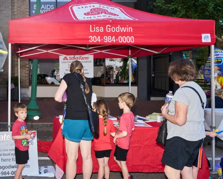Two adults and three children are seen at a vendor table. A popup tent above them reads, "Lisa Godwin, 304-984-0000."