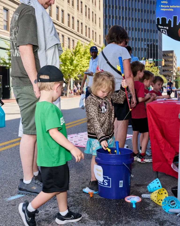 Two children stand around a bucket outside on a sunny day.