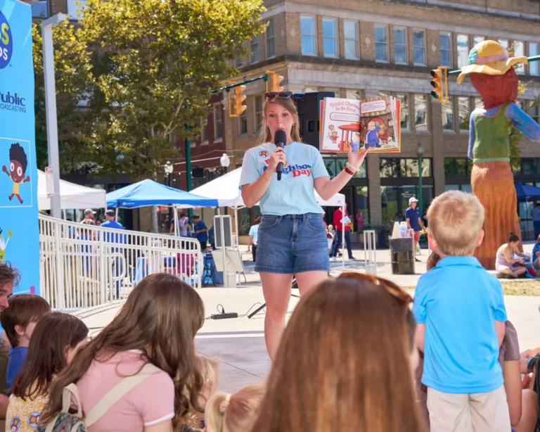 A woman reads a book to children sitting on the ground.