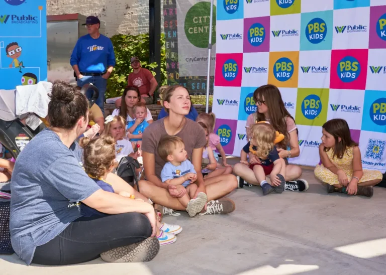 Families sit on the ground and listen to a storybook read aloud.