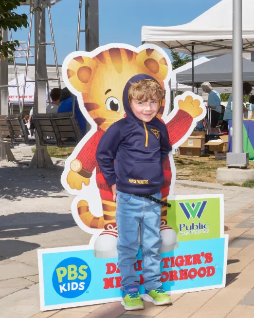 A young boy smiles and poses for a photo in front of a Daniel Tiger cutout.