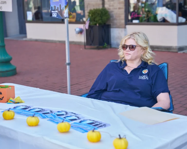 A woman sits at a vendor table and looks on.