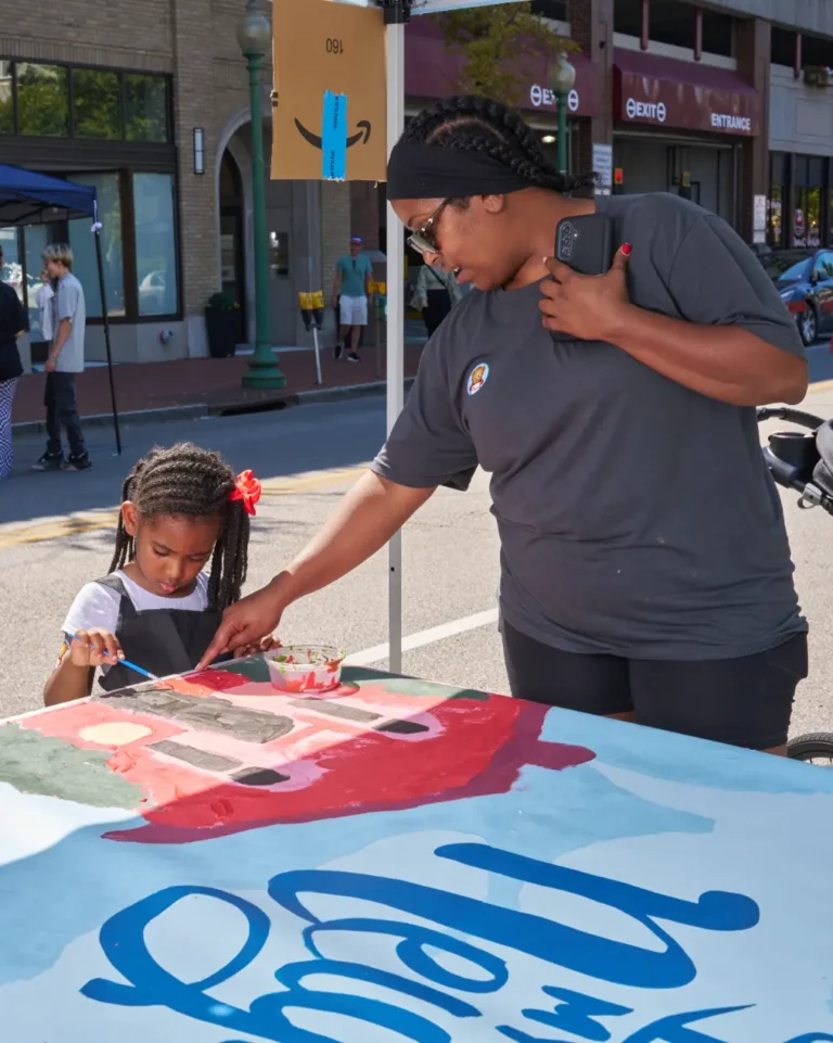 A woman helps a young girl paint a mural.